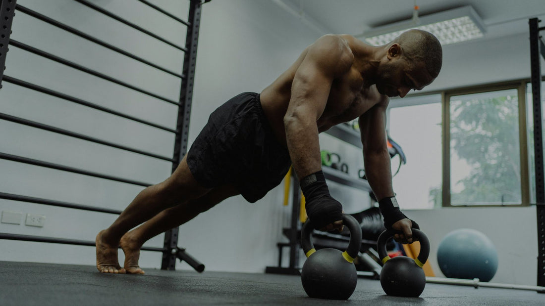 Muscular man performing advanced push ups using two kettlebells in gym