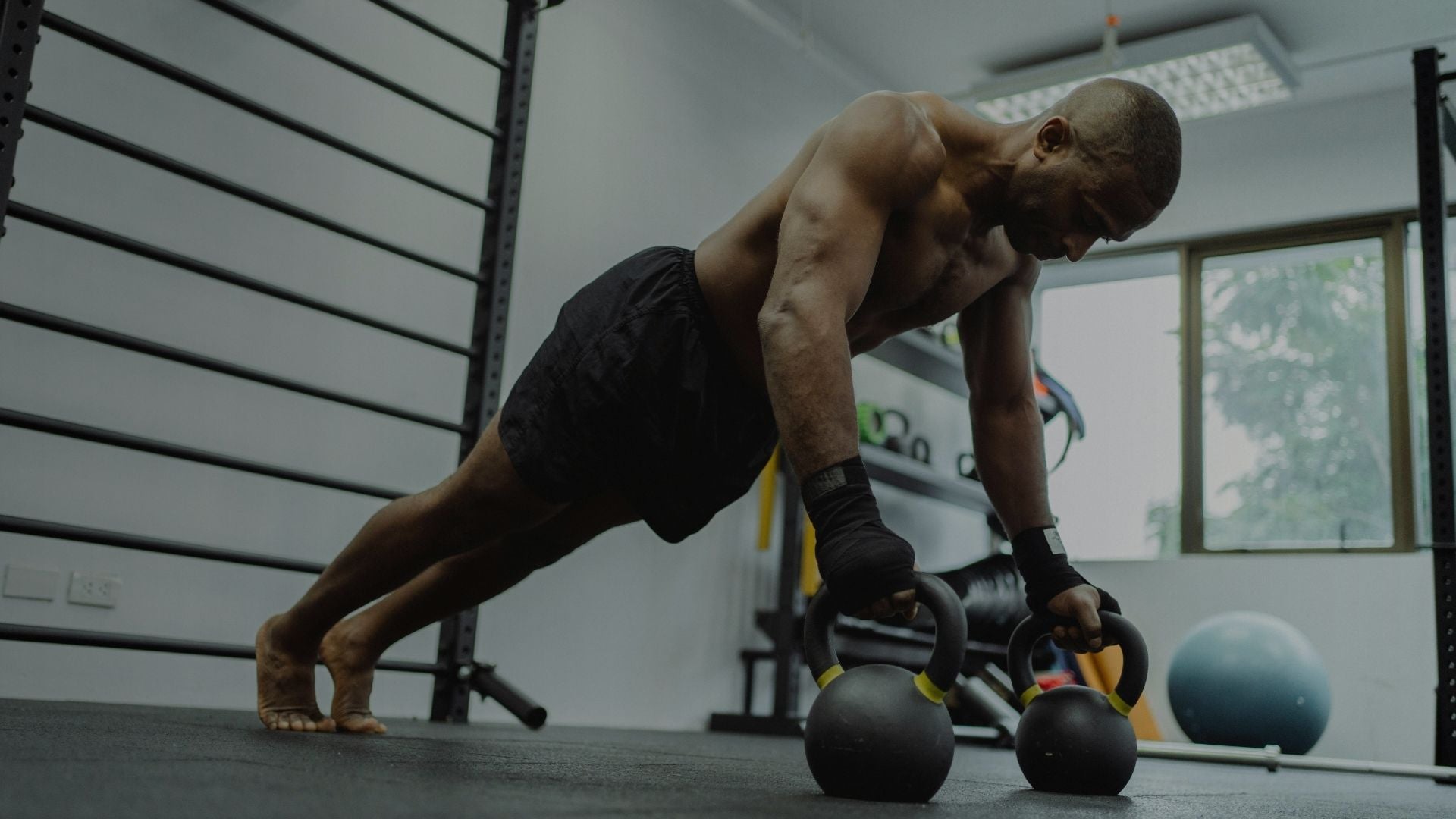 Muscular man performing advanced push ups using two kettlebells in gym